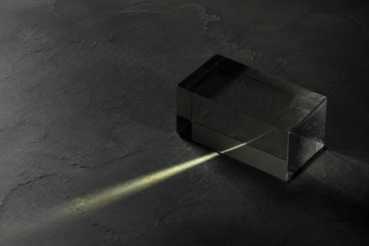 Light refracting through a glass prism on a dark stone surface